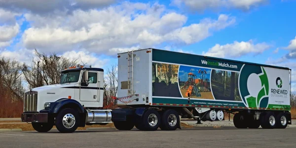 A large truck with a scenic landscape mural on its trailer is parked under a partly cloudy sky.