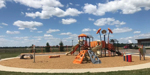 A colorful playground under a blue sky with scattered clouds.